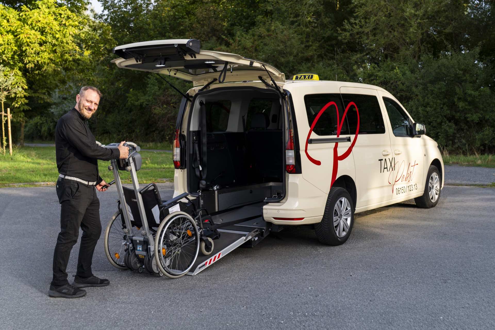 Ein Fahrer von Taxi Pabst mit Beförderungsstuhl an der Rollstuhlrampe des Taxis